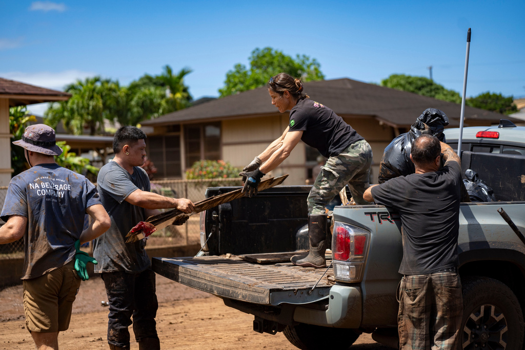 Volunteers load debris and damaged household items onto a truck during cleanup efforts following flooding, Tuesday, March 24, 2026, in Waialua, Hawaii. (AP Photo/Mengshin Lin)