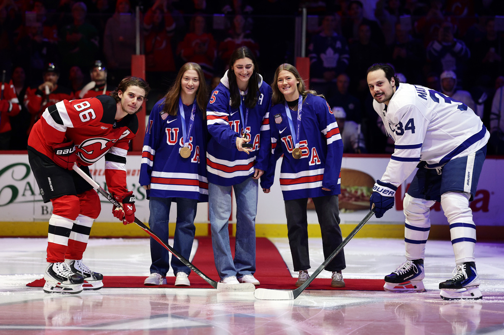 United States women's gold medal hockey players, center left to right, Aerin Frankel, Megan Keller and Haley Winn with New Jersey Devils center Jack Hughes (86) and Toronto Maple Leafs center Auston Matthews (34) for a ceremonial puck drop before an NHL hockey game Wednesday, March 4, 2026, in Newark, N.J. (AP Photo/Adam Hunger)