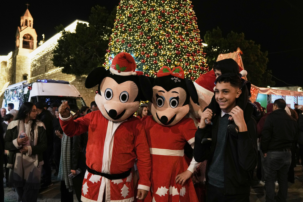 Palestinians pose for the pictures with performers in Manger Square in the West Bank city of Bethlehem, Friday, Dec. 12, 2025. (AP Photo/Mahmoud Illean)