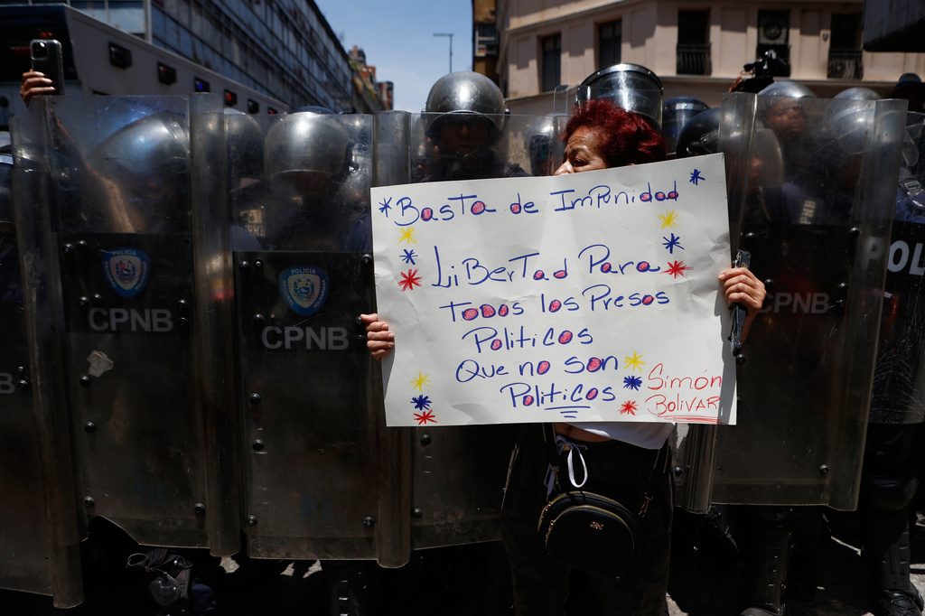 A protester holds up a sign demanding freedom for all political prisoners as she stands in front of a cordon of Bolivarian National Police, during a march demanding higher salaries, pensions and benefits, in Caracas, Venezuela, Thursday, April 9, 2026. (AP Photo/Pedro Mattey)