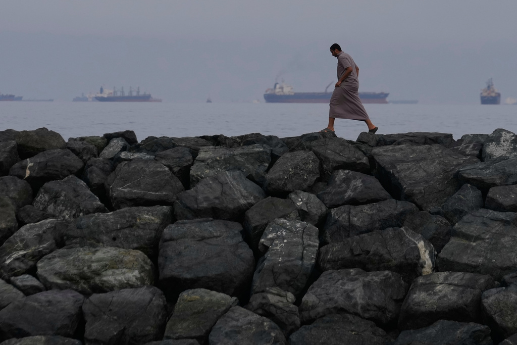 A man walks along the shore as oil tankers and cargo ships line up in the Strait of Hormuz, as seen from Khor Fakkan, United Arab Emirates, Wednesday, March 11, 2026. (AP Photo/Altaf Qadri)