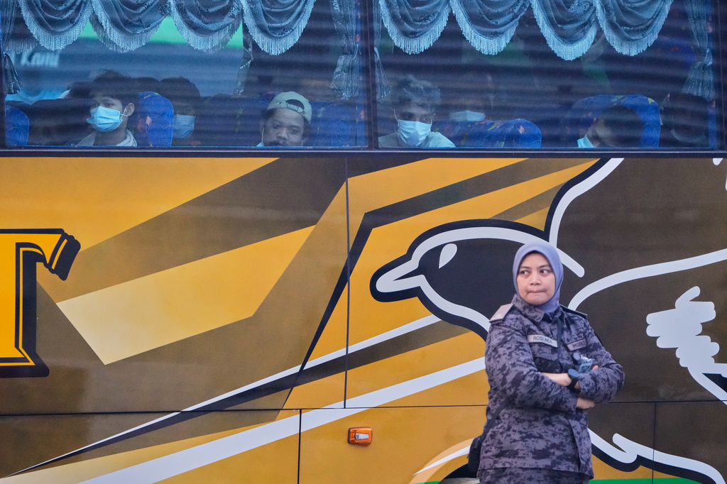 Myanmar nationals look out from a bus in Manjung, Perak state of Malaysia, on Tuesday, Sept. 29, 2026, as a uniformed official walks past. (AP Photo/Vincent Thian)