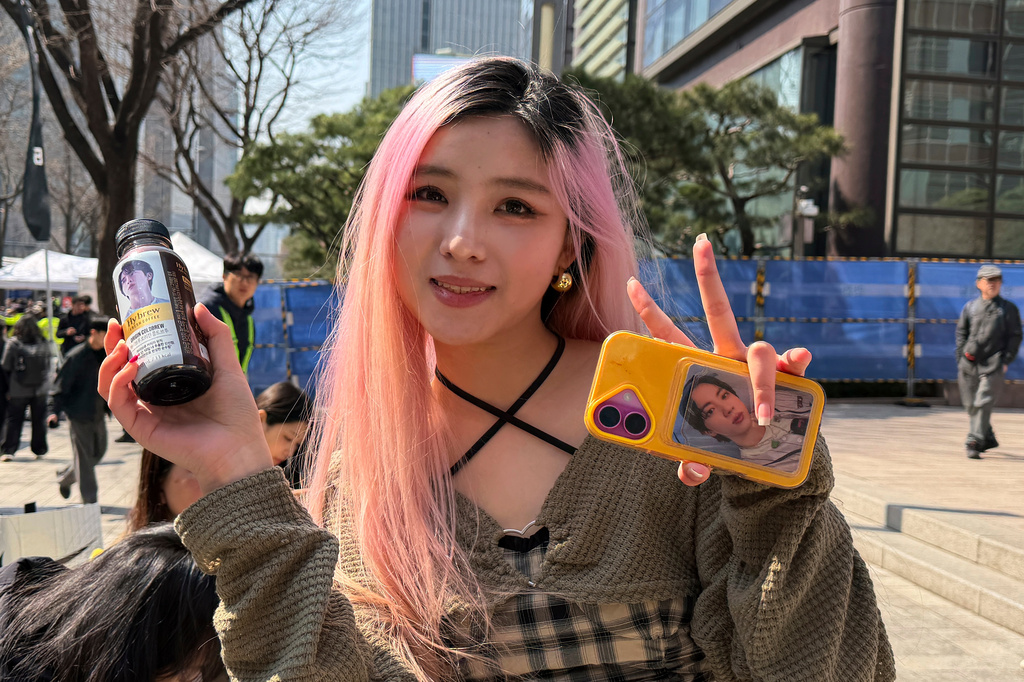 BTS fan Wang Yuchen from Sichuan province in China poses for a photo while holding BTS merchandise ahead of BTS's comeback concert near Gwanghwamun Square in Seoul, South Korea, Saturday, March 21, 2026. (AP Photo/ Juwon Park)