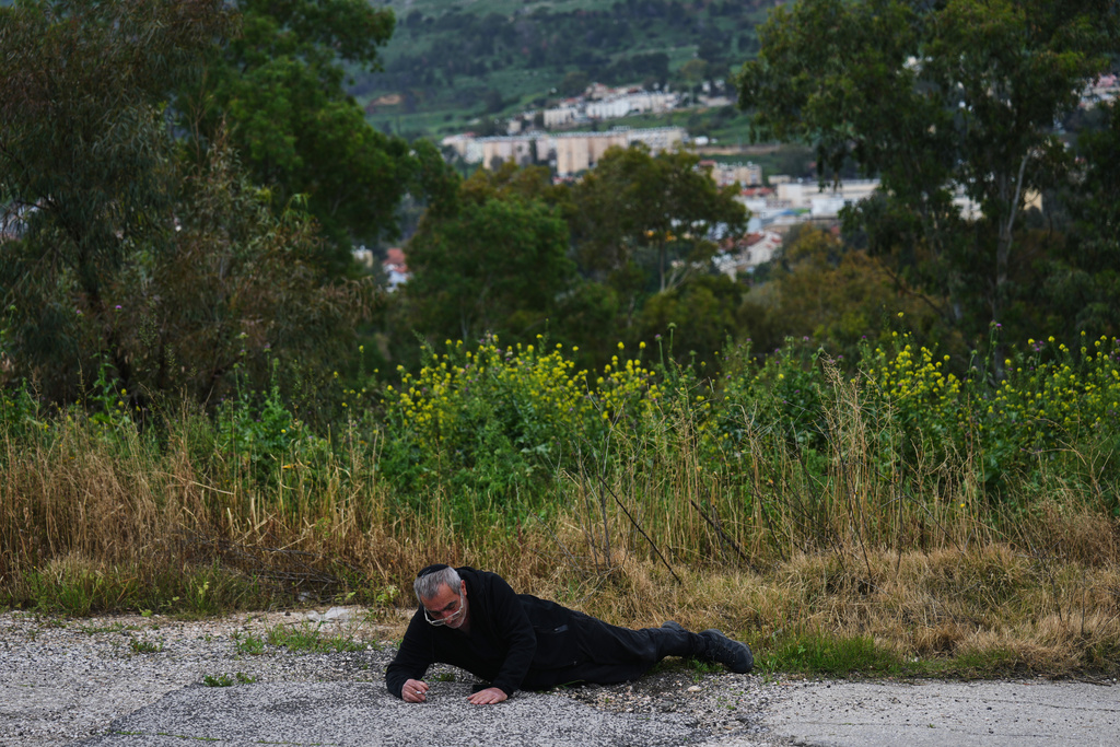 A man takes cover as air raid sirens sound, warning of rockets launched from Lebanon toward Israel, in Kiryat Shmona, northern Israel, Monday, March 23, 2026. (AP Photo/Ariel Schalit)