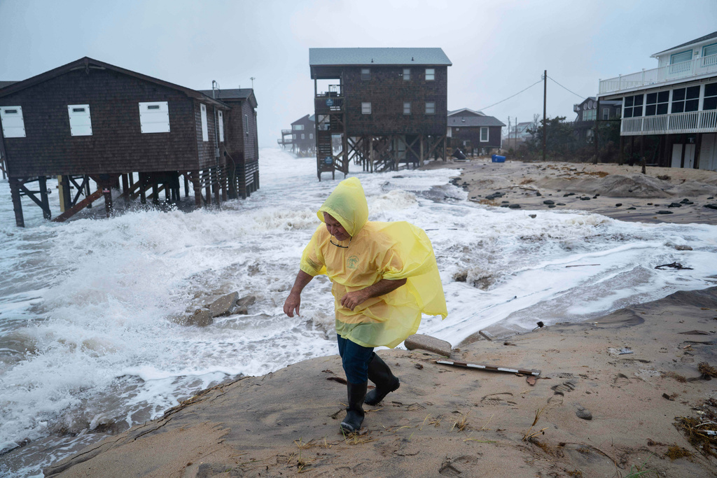 A man walks past houses at risk of collapse in the midst of a storm, Sunday, Oct. 12, 2025, in Buxton, N.C. (AP Photo/Allison Joyce)