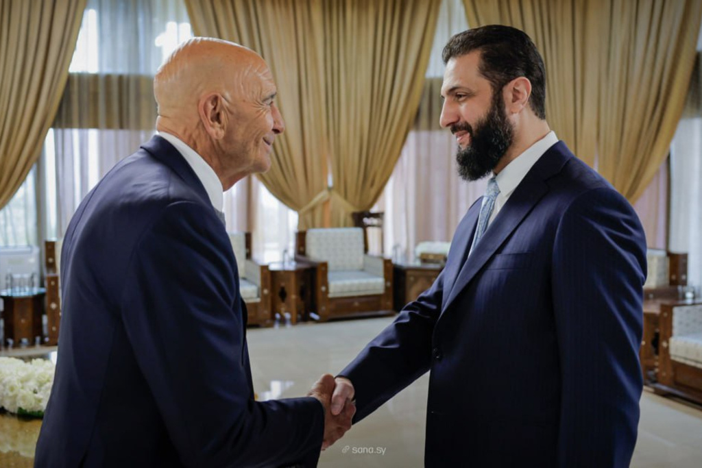 In this photo released by the Syrian official news agency SANA, U.S. Ambassador to Turkey and Special Envoy to Syria Tom Barrack, left, shakes hands with Syria's President Ahmad al-Sharaa, in Damascus, Syria, Sunday, Jan. 18, 2026. (SANA via AP)