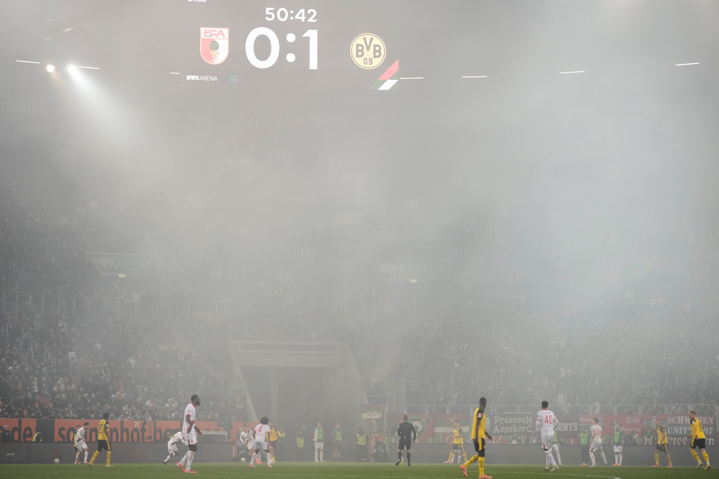 Smoke floats over the pitch during the Bundesliga soccer match between FC Augsburg and Borussia Dortmund in Augsburg, Germany, Friday, Oct. 31, 2025. (AP Photo/Matthias Schrader)