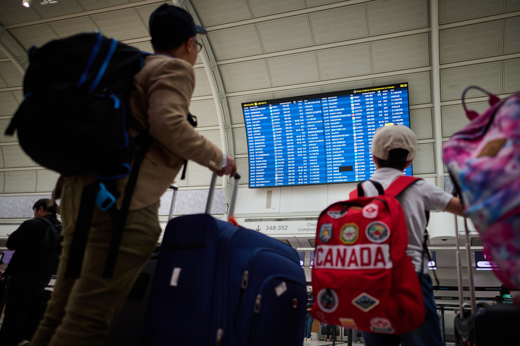 Travelers look at departures by the WestJet gate as the airline's flight attendants strike outside at Pearson International Airport in Toronto, on Sunday, Aug. 2, 2026. (Sammy Kogan/The Canadian Press via AP)