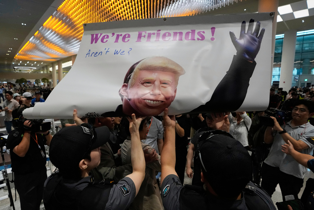 Protesters try to hold a banner depicting U.S. President Donald Trump as police officers and members of airport security block at the arrival terminal of the Incheon International Airport, in Incheon, South Korea, Friday, Sept. 12, 2025. (AP Photo/Ahn Young-joon)