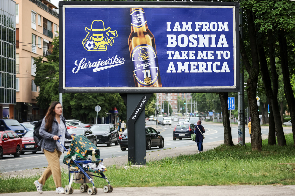 A woman walks past a billboard displaying lyrics from the Dubioza kolektiv song "I Am From Bosnia, Take Me to America" in Sarajevo, Bosnia, Thursday, June 11, 2026. (AP Photo/Armin Durgut)