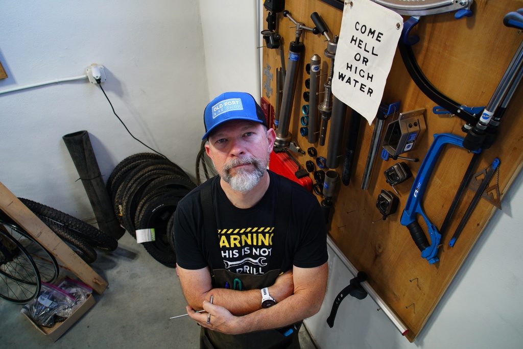 Chad Schoenauer poses for a portrait beneath a sign that reads "Come Hell or High Water" in his bike shop in Old Fort, N.C., on Thursday, Sept. 1, 2025. (AP Photo/Allen G. Breed)