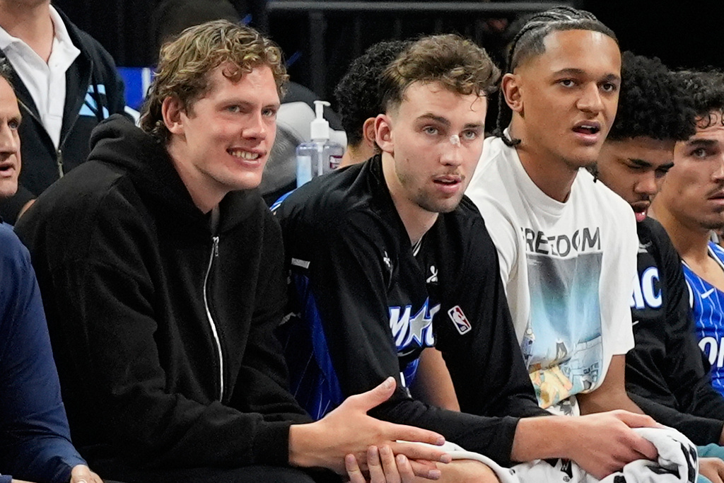**HOLD FOR STORY BY ROB MADDIE**Orlando Magic players and brothers Moritz Wagner, left, and Franz Wagner, center, watch the first half of an NBA basketball game with teammate Paolo Banchero against the Golden State Warriors, Tuesday, Nov. 18, 2025, in Orlando, Fla. (AP Photo/John Raoux)