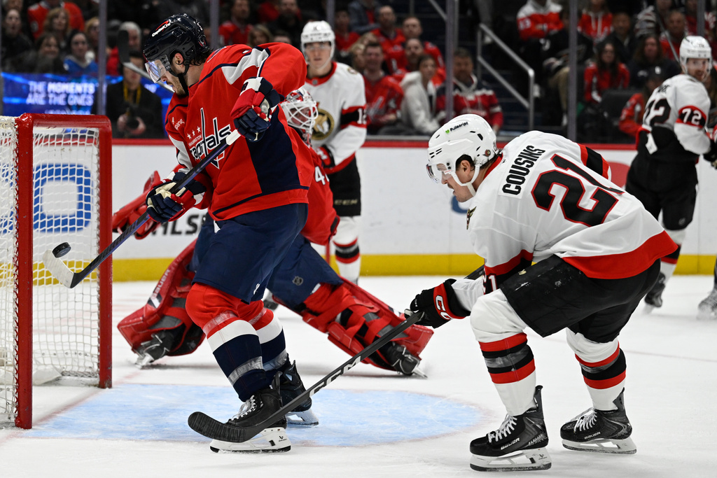 Washington Capitals defenseman Matt Roy, left, bats the puck away from a goal in front of Ottawa Senators center Nick Cousins during the second period of an NHL hockey game, Wednesday, March 18, 2026, in Washington. (AP Photo/John McDonnell)