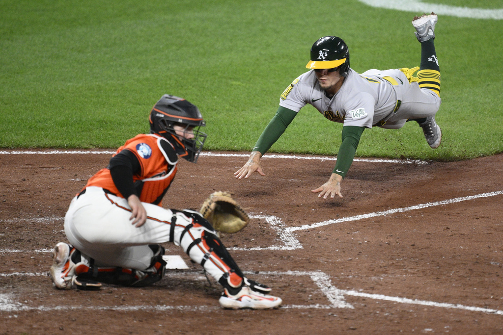 Athletics' Luis Urías, right, dives toward home to score against Baltimore Orioles catcher Adley Rutschman, left, on a double by Gio Urshela during the fifth inning of a baseball game, Saturday, Aug. 9, 2025, in Baltimore. (AP Photo/Nick Wass)