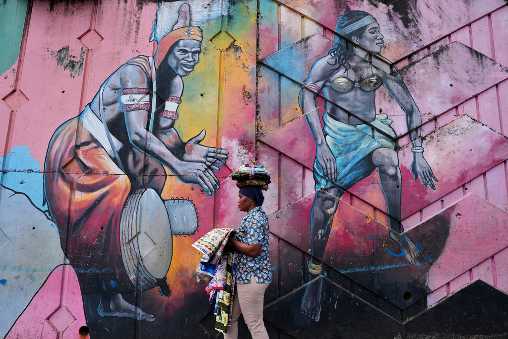 A street vendor walks past a mural depicting traditional dancers on a street wall in Conakry, Guinea, Saturday, Sept. 20, 2025. (AP Photo/Misper Apawu)