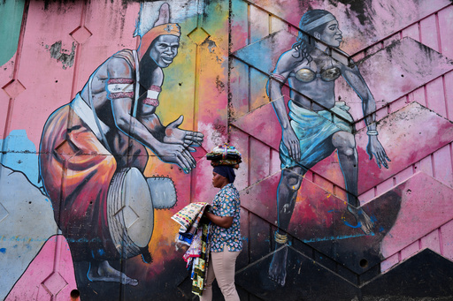 A street vendor walks past a mural depicting traditional dancers on a street wall in Conakry, Guinea, Saturday, Sept. 20, 2025. (AP Photo/Misper Apawu) A street vendor walks past a mural depicting traditional dancers on a street wall in Conakry, Guinea, Saturday, Sept. 20, 2025. (AP Photo/Misper Apawu)