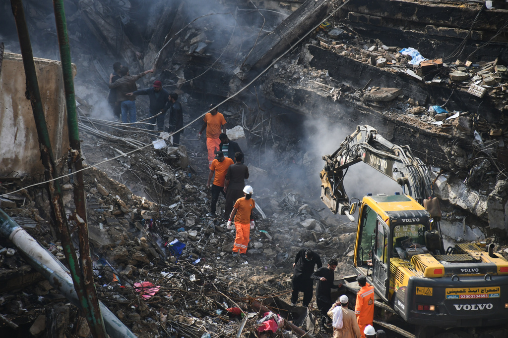 Rescue workers and firefighters with heavy machinery conduct a search operation at a burnt building of a multi-story shopping plaza following a massive fire in Karachi, Pakistan, Wednesday, Jan. 21, 2026. (AP Photo/Ali Raza)