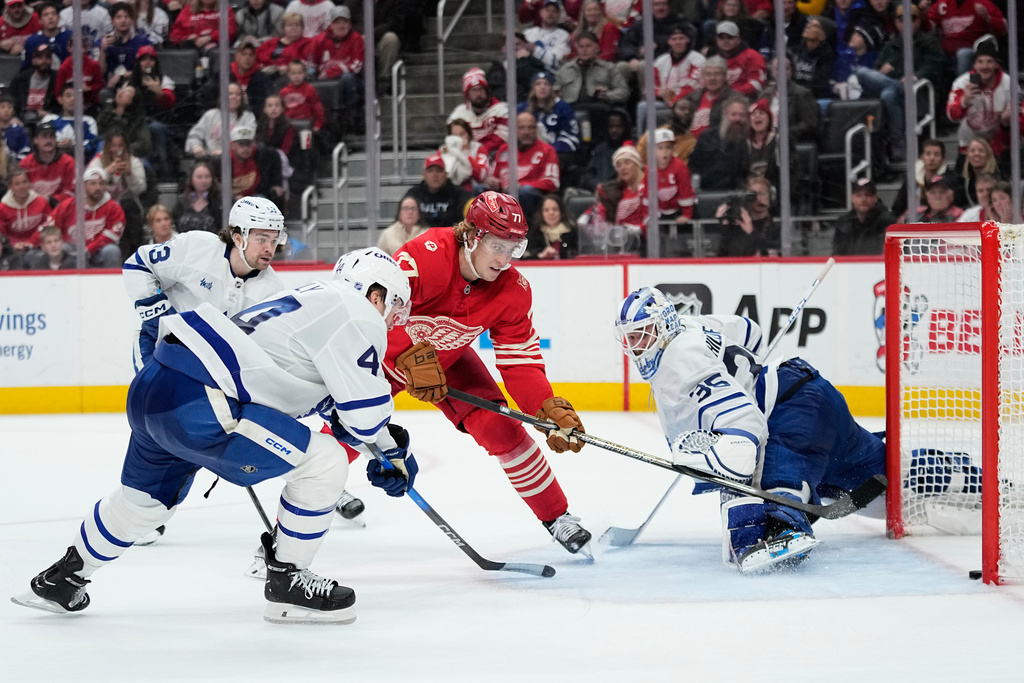 Detroit Red Wings defenseman Simon Edvinsson, third from left, scores the winning goal against Toronto Maple Leafs right wing Easton Cowan, left, defenseman Morgan Rielly, second from left, and goaltender Dennis Hildeby, right, during overtime of an NHL hockey game Sunday, Dec. 28, 2025, in Detroit. (AP Photo/Ryan Sun)