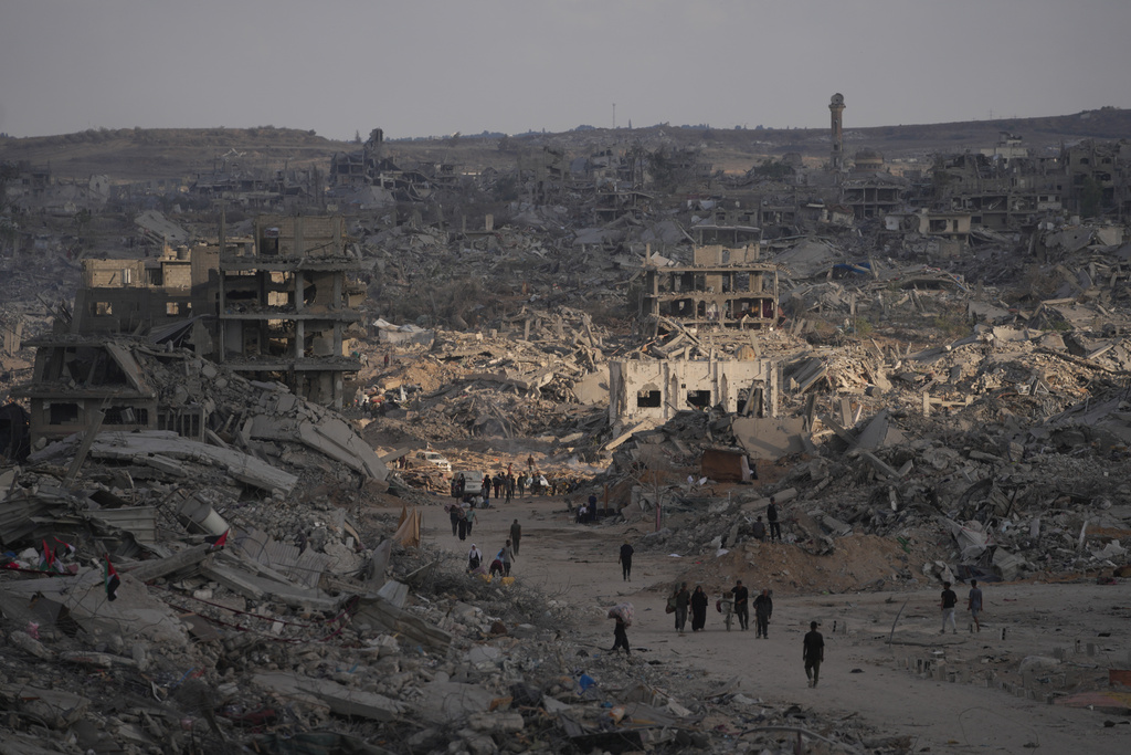 Palestinians walk among destroyed buildings in Gaza City, Sunday, Oct. 12, 2025, after Israel and Hamas agreed to a pause in their war and the release of the remaining hostages. (AP Photo/Jehad Alshrafi)