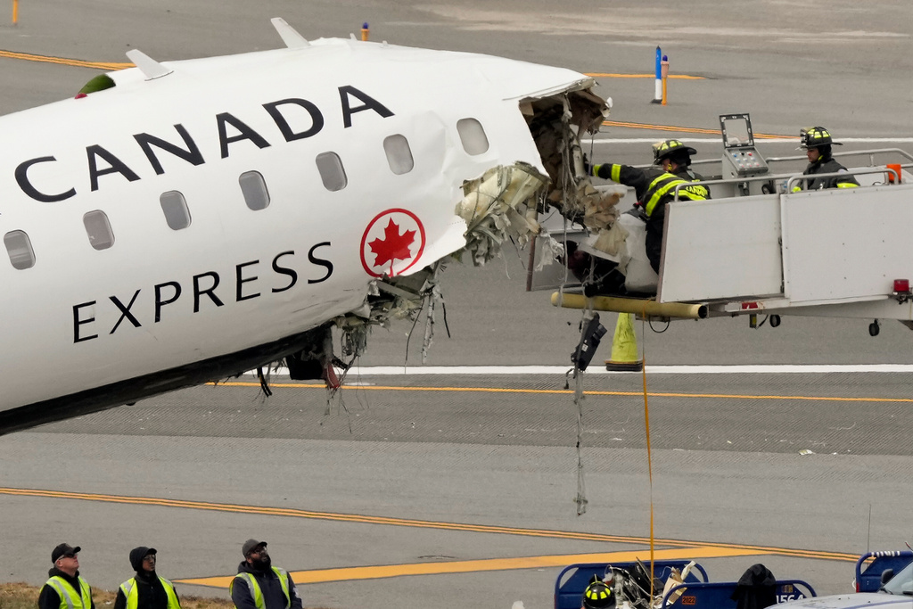 Airport firefighters remove loose debris from the wreckage of an Air Canada Express jet, Wednesday, March 25, 2026, just off the runway where it had collided with a Port Authority fire truck Sunday night at LaGuardia Airport in New York. (AP Photo/Yuki Iwamura)