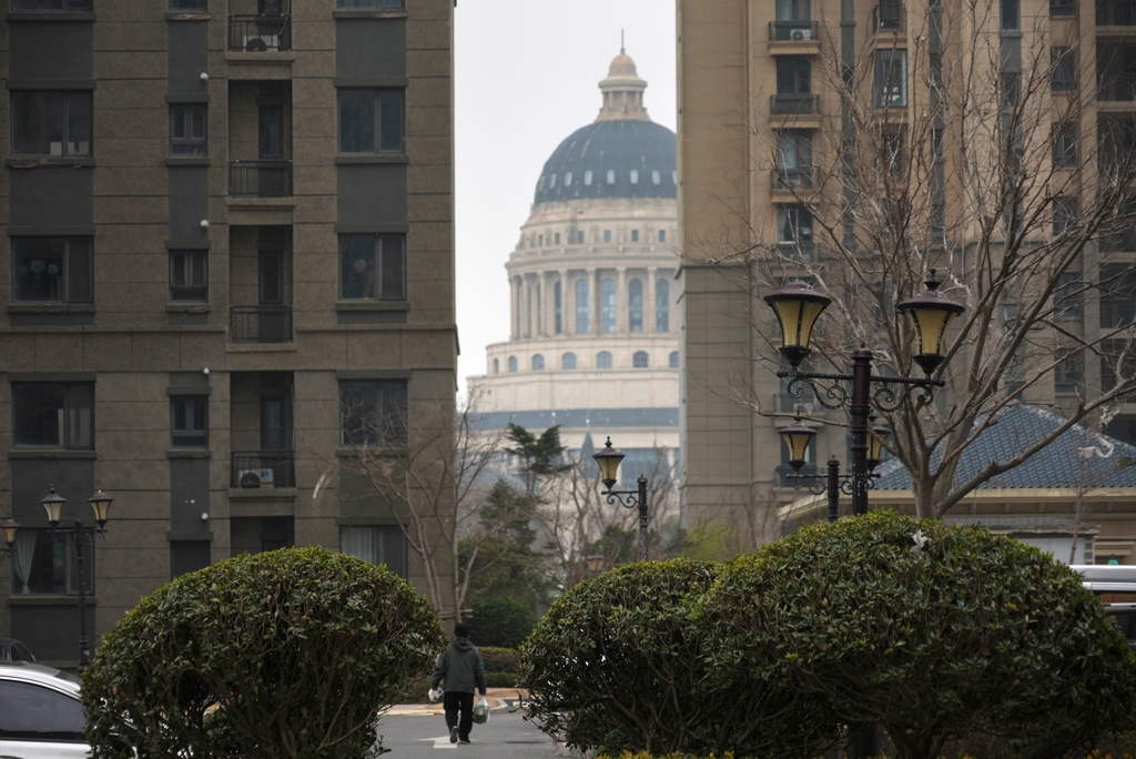 A resident carries groceries under the shadow of the massive dome of the International Conference Center of the semi-abandoned "Life in Venice" housing complex in Qidong, on China's east coast, Feb. 5, 2026. (AP Photo/Dake Kang)