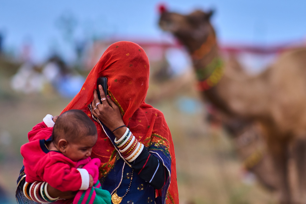 A woman holds her child as she talks on a phone at the annual cattle fair in Pushkar, in the western Indian state of Rajasthan, Sunday, Oct. 26, 2025. (AP Photo/Rajesh Kumar Singh)