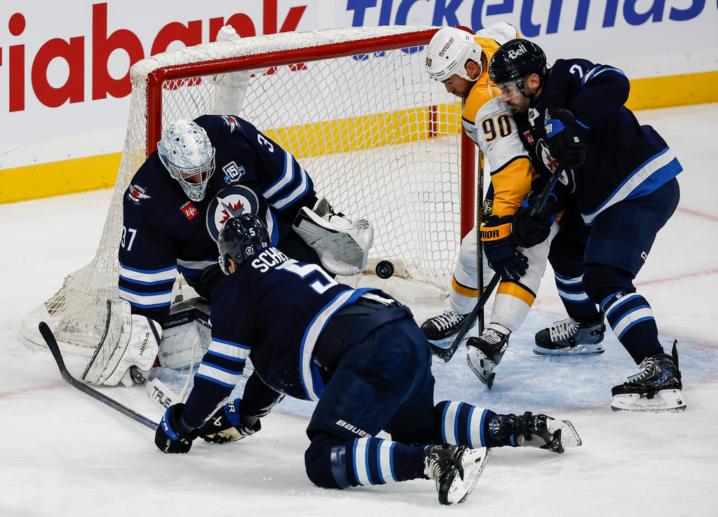 Winnipeg Jets goaltender Connor Hellebuyck (37) saves a shot as teammates Luke Schenn (5) and Dylan DeMelo (2) defend against Nashville Predators' Ryan O'Reilly (90) during second-period NHL hockey game action in Winnipeg, Manitoba, Saturday, Oct. 18, 2025. (John Woods/The Canadian Press via AP)