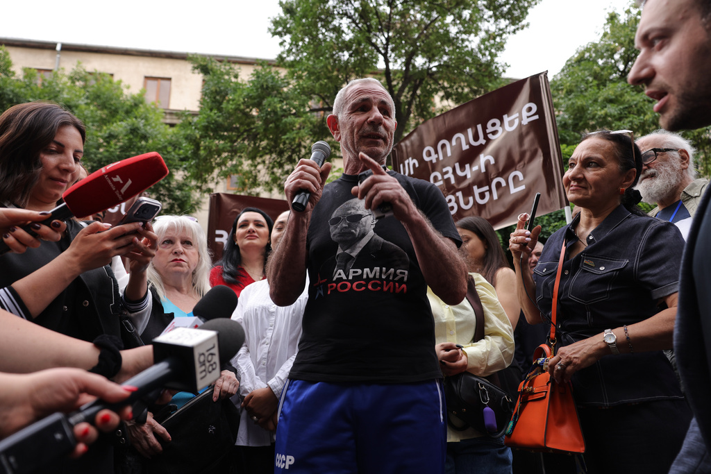 A man wearing in t-shirt with an image of Russian President Vladimir Putin and words reading "Army of Russia" gestures speaking to demonstrators of opposition parties gathered in protest of the results of the parliamentary elections in Yerevan, Armenia, Sunday, June 14, 2026. (AP Photo/Anthony Pizzoferrato)