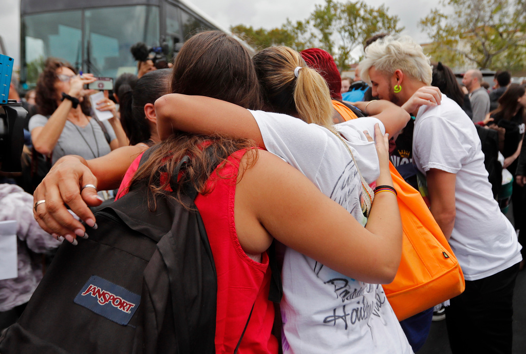 FILE - Students who survived the shooting at Stoneman Douglas High School hug survivors of the Pulse nightclub shooting before boarding buses in Parkland, Fla., Feb. 20, 2018, to rally outside the state capitol and talk to legislators about gun control reform. (AP Photo/Gerald Herbert, File)