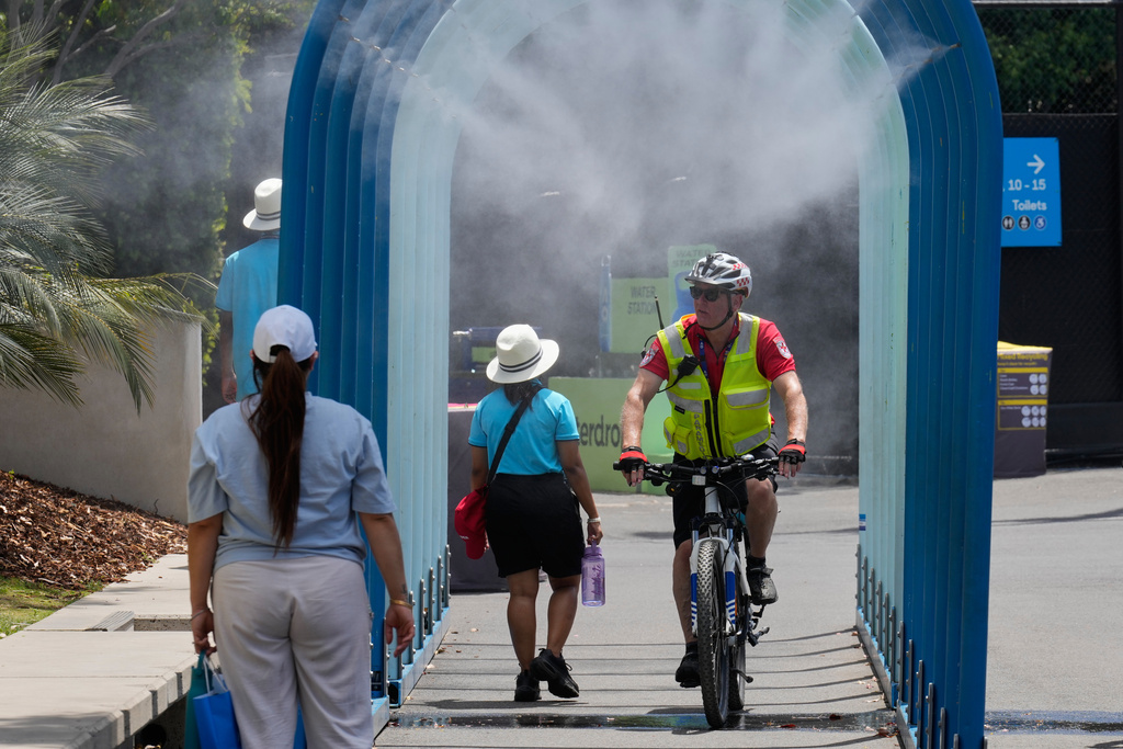 Fans walk and ride bikes through a water mister at the Australian Open tennis championship in Melbourne, Australia, Tuesday, Jan. 27, 2026. (AP Photo/Dar Yasin)
