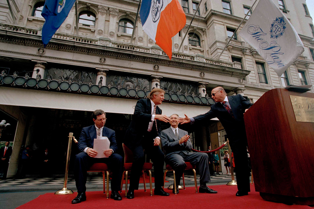 FILE - Donald Trump, second from left and former owner of the Plaza Hotel, reaches to shake the hand of Robert Small, right, CEO of Fairmont Hotel Management at a flag raising ceremony at the Plaza Hotel, July 28, 1995. (AP Photo/Adam Nadel, File)