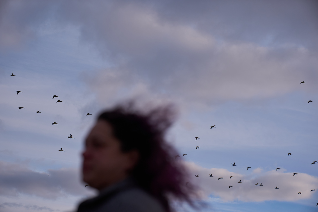Birds fly above as Jean Booth, who was targeted in a romance scam, walks on the beach in Huron, Ohio, Dec. 8, 2025. (AP Photo/David Goldman)