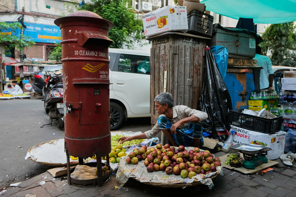A government postal department letterbox stands on a street corner as a person sells fruit on the pavement in Kolkata, Tuesday, April 21, 2026. (AP Photo/Bikas Das)