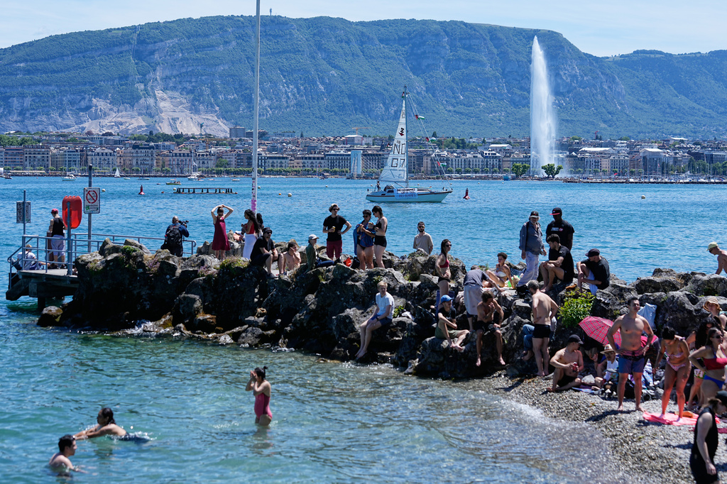 People gather and swim on Lake Geneva, Switzerland, as a sailboat with a "No G7" banner sails by, Sunday, June 14, 2026, ahead of the G7 summit scheduled to take place in France June 15-17. (AP Photo/Laurent Cipriani)