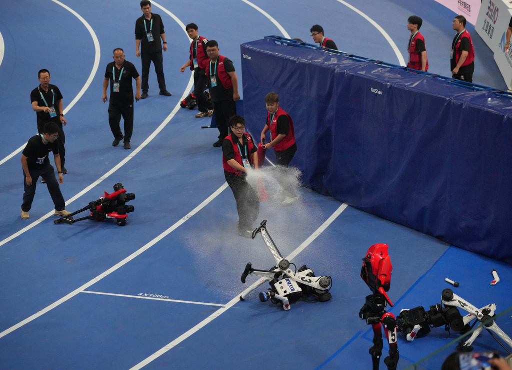Official extinguish the fire to a Humanoid robot after hitting the barrier at the end of the 100m race during the World Humanoid Robot Games in Beijing, Tuesday, Aug. 25, 2026. (AP Photo/Achmad Ibrahim)