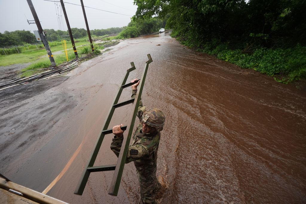 A member of Hawaii Army National guard removes a ladder from a vehicle as rainwater from nearby Hurricane Nolo floods a section of Mamalahoa highway Saturday, Sept. 26, 2026, near Naalehu, Hawaii. (AP Photo/Gregory Bull)