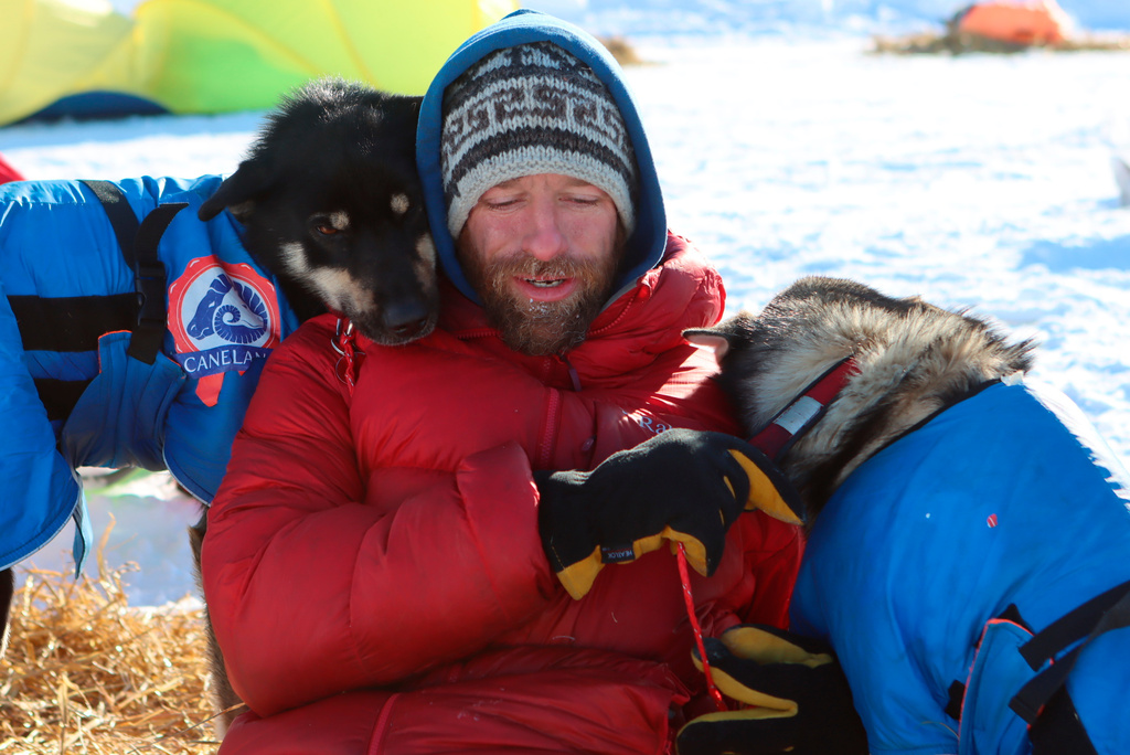FILE - Musher Jessie Holmes takes a break from cooking his dogs a meal to nuzzle with two wheel dogs at the Ophir checkpoint during the Iditarod Trail Sled Dog Race, March 10, 2021, in Alaska. (Zachariah Hughes/Anchorage Daily News via AP, Pool, File)