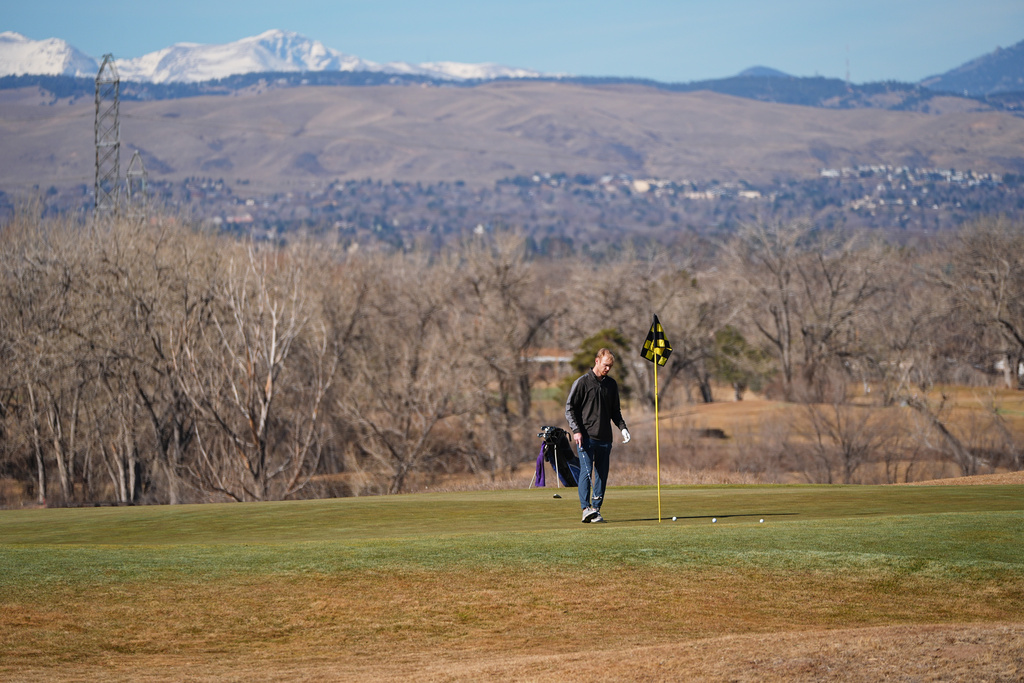 With little snow covering the mountain backdrop, a lone golfer putts out on a green on the Broken Tee Golf Course, Friday, Feb. 6, 2026, in Sheridan, Colo. (AP Photo/David Zalubowski)
