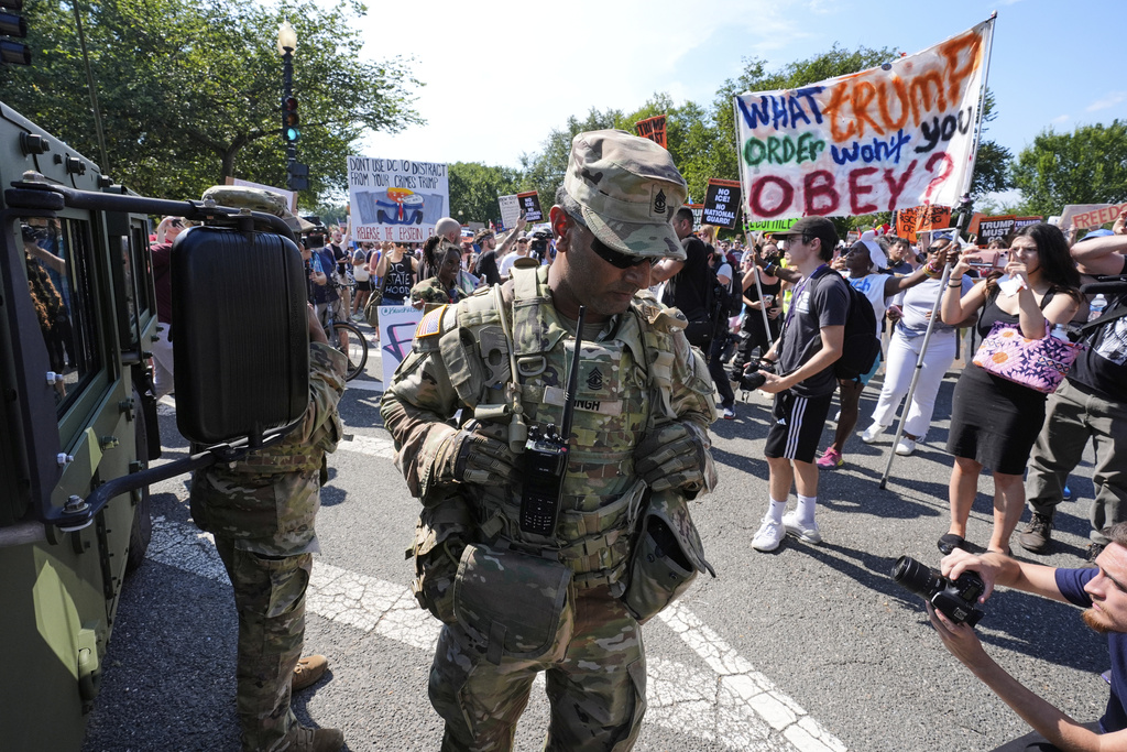 A first sergeant with the District of Columbia National Guard watches as activists protest President Donald Trump's federal takeover of policing of the District of Columbia, Saturday, Aug. 16, 2025, in Washington. (AP Photo/Alex Brandon)