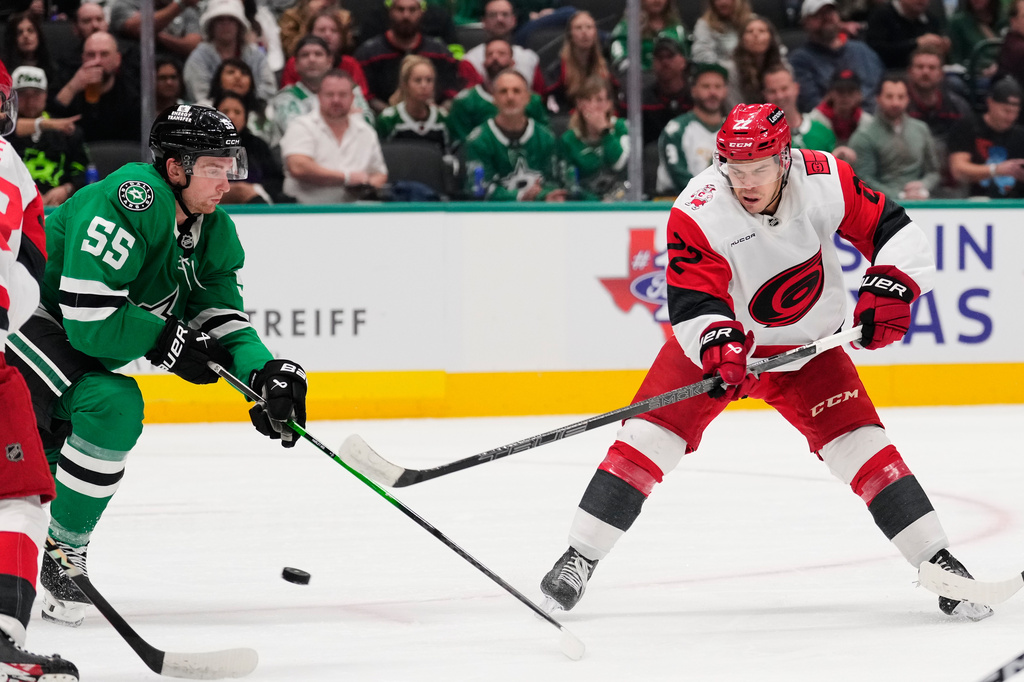 Carolina Hurricanes' Logan Stankoven (22) flips the puck to the front of the net as Dallas Stars' Thomas Harley (55) defends in the second period of an NHL hockey game Saturday, Oct. 25, 2025, in Dallas. (AP Photo/Tony Gutierrez)