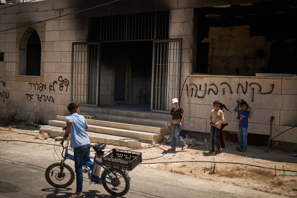 Children stand outside a mosque that was burned during an attack by Israeli settlers early in the morning in the West Bank village of Qusra, Sunday, July 26, 2026, as on its wall a Hebrew graffiti reads "Revenge Benayahu", referring to an Israeli settler killed during clashes with Palestinians in the village of Tell, last Friday. (AP Photo/Leo Correa)