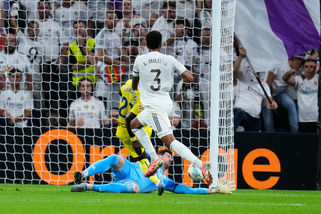 Real Madrid's goalkeeper Thibaut Courtois, left, and Eder Militao, right, challenge as Villarreal's Tani Oluwaseyi shoots on goal during the Spanish La Liga soccer match between Real Madrid and Villarreal at the Santiago Bernabeu stadium in Madrid, Spain, Saturday, Oct. 4, 2025. (AP Photo/Manu Fernandez)