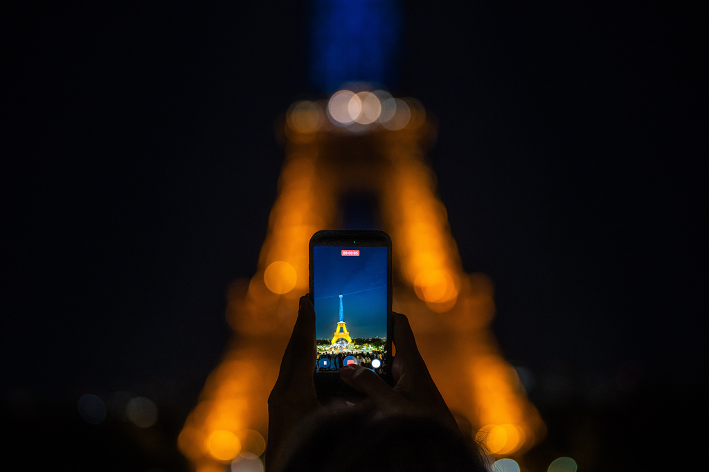 A man takes a photo of the Eiffel Tower illuminated with the colors of Ukraine in honor of it's Independence Day and to mark the fourth anniversary of Russia's invasion of the country, in Paris, Monday, Aug. 24, 2026. (AP Photo/Aurelien Morissard)