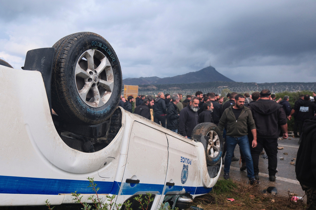 Farmers gather next to an overturned police vehicle during clashes with officers blocking their march to Chania's airport on Crete, Greece, Monday, Dec. 8, 2025, amid protests over delayed EU farm subsidies. (AP Photo/Giannis Angelakis)