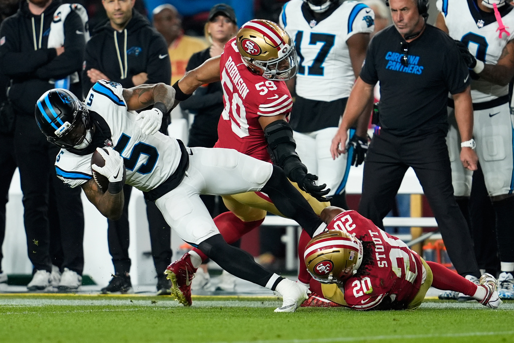 Carolina Panthers running back Rico Dowdle is tackled by San Francisco 49ers linebacker Curtis Robinson (59) and cornerback Upton Stout (20) during the first half an NFL football game, Monday, Nov. 24, 2025, in Santa Clara, Calif. (AP Photo/Godofredo A. Vásquez)