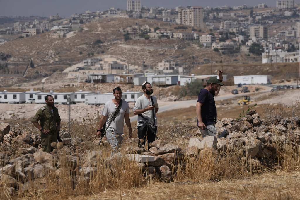 Israeli settlers gather from a nearby outpost, background, after Israeli and foreign peace activists took down a metal structure in the shape of a Star of David from atop a Palestinian structure during a protest in support of local landowners whose property is threatened with seizure by settlers, on the outskirts of the West Bank city of Beit Sahour, Friday, Aug. 14, 2026. (AP Photo/Mahmoud Illean)
