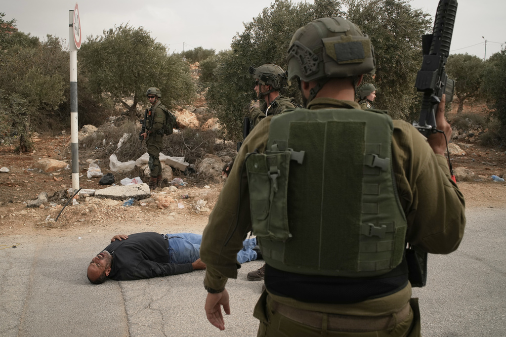 Israeli soldiers stand beside a wounded Palestinian man lying on a road after soldiers shot him following a settler attack on Palestinians harvesting olives in the occupied West Bank village of Abu Falah, Friday, Oct. 16, 2026. (AP Photo/Leo Correa)
