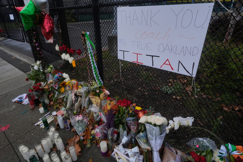 Flowers and signs are displayed at a sidewalk memorial for former Oakland football coach John Beam at Laney College, in Oakland, Calif., Monday, Nov. 17, 2025. (AP Photo/Jeff Chiu)