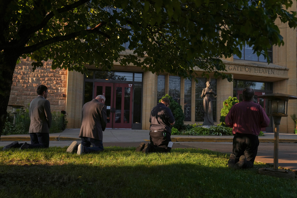 People kneel by the Annunciation Catholic Church after Wednesday's school shooting, Thursday, Aug. 28, 2025, in Minneapolis. (AP Photo/Abbie Parr)