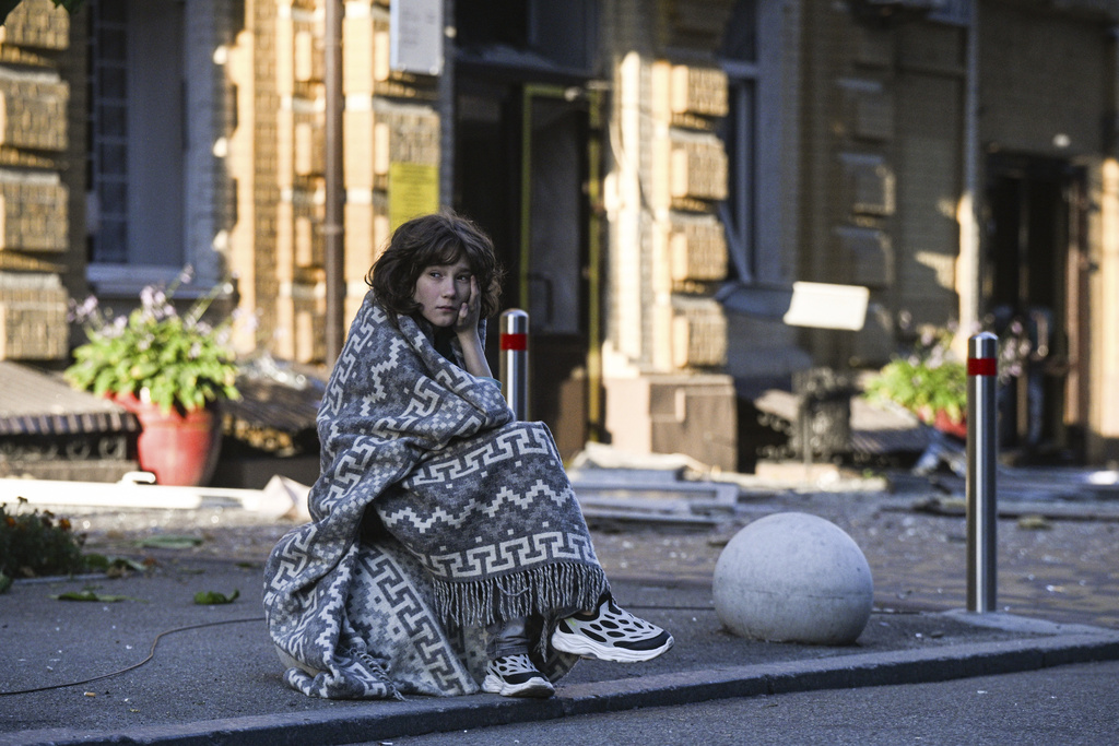 A young woman wrapped in a blanket sits in the street after her home was damaged in Russia's drone and missile attack in central Kyiv, Ukraine, Thursday, Aug. 28, 2025 (AP Photo/Danylo Antoniuk)